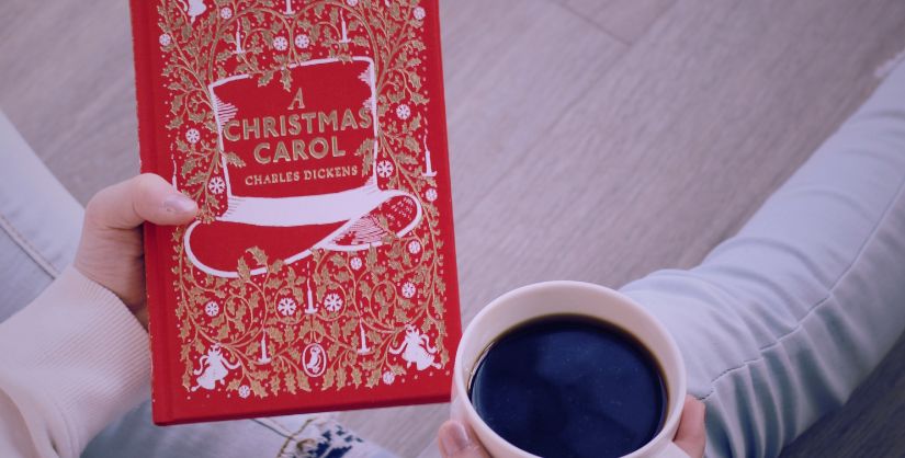 Person with A Christmas Carol Book in their hand and a coffee.